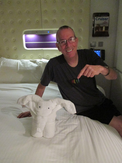 Photo shows Gene sitting on his bed and smiling, pointing to a small white terry-cloth elephant.